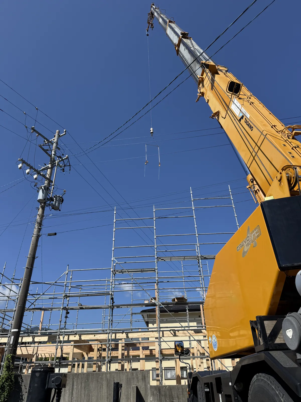 茅野市の建て方現場で架空線近くに旋回する16tクレーンのブーム